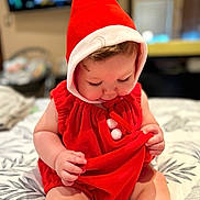 Noah is registered to the contest to win money with this photo: baby, bedspread, child, chubby_cheeks, cozy, curious, cute, face, hands, hood, indoors, infant, legs, long_eyelashes, pattern, pom_poms, red_clothing, sitting, skin, soft_fabric