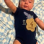 baby, infant, onesie, blue, blanket, wooden_plaque, 4_months, dinosaur_print, smiling, lying_down, arm_raised, cute, soft_texture, skin, child, young, indoors, plush, happy, portrait