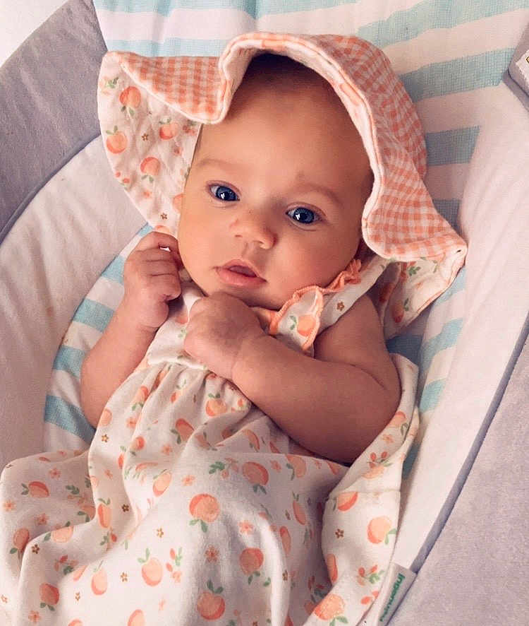 Nevaeh is registered to the contest to win money with this photo: baby, infant, blue_eyes, hat, dress, peach_pattern, bassinet, blanket, cute, child, sleeping_area, soft, clothing, portrait, newborn, resting, indoors, comfort, toddler, adorable