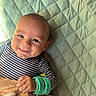 baby, smiling, striped_clothing, blanket, quilted, stuffed_animal, hand, face, child, infant, cute, happy, lying_down, soft_toy, green, blue, striped, portrait, indoors, closeup
