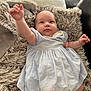 baby, blue_dress, child, couch, cozy, cute, dress, fluffy_rug, hand, head, indoor, infant, lying_down, person, portrait, raising_arm, skin, smiling, soft_texture, young_child