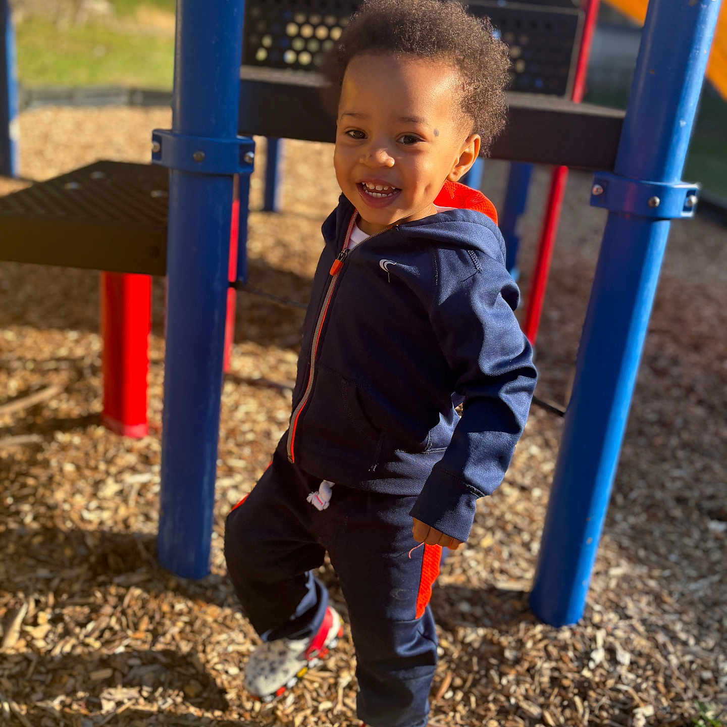 Noah joined the competition — help win amazing prizes! active, casual_clothing, child, cute, daylight, dimples, fun, happy, outdoor, person, play_equipment, playground, shoes, smiling, standing, sunny, toddler, tracksuit, woodchips, young_child