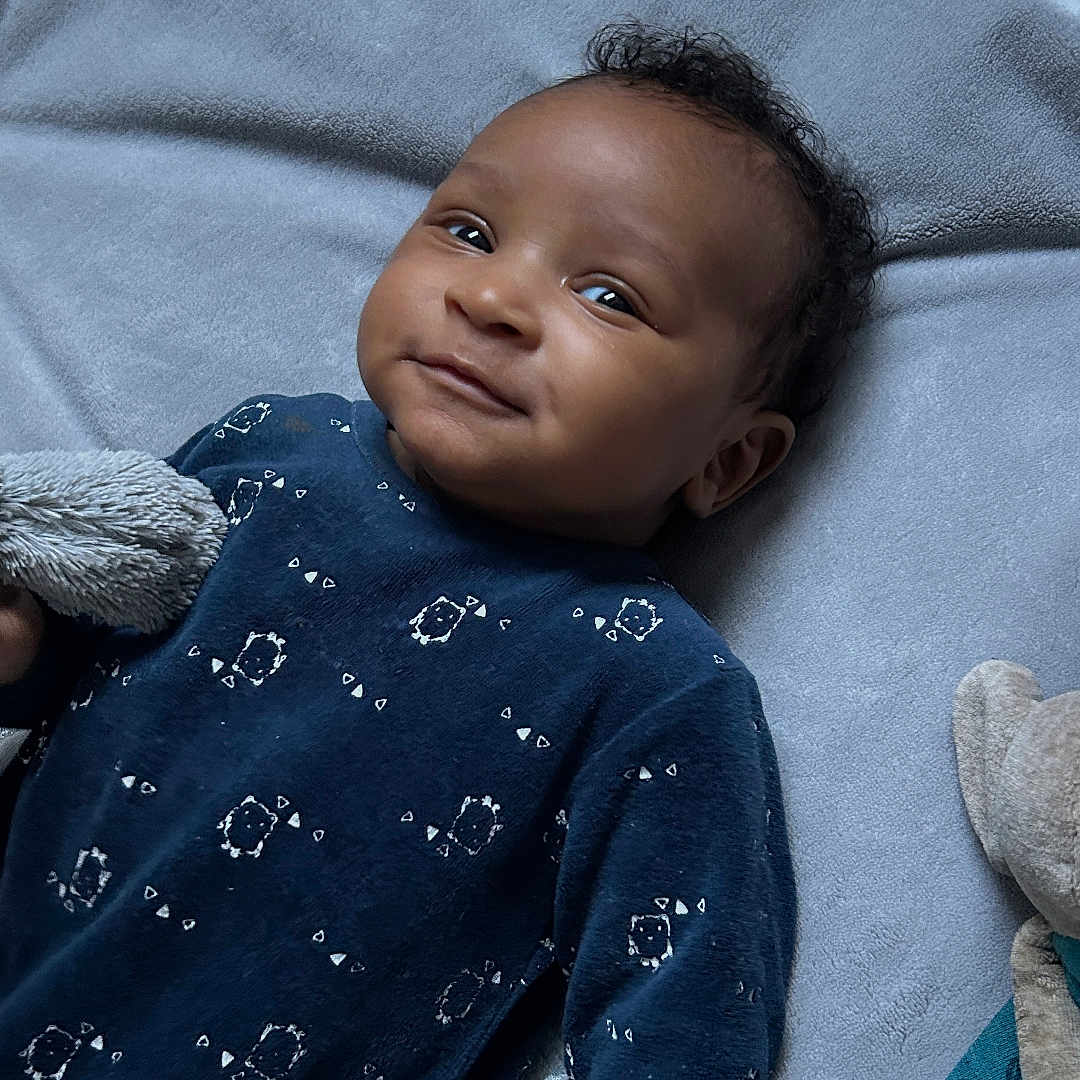 Nyliane participe au concours pour gagner de l'argent avec cette photo : baby, blue_clothing, child, cozy, curly_hair, cute, face, floor, hand, indoor, infant, lying_down, patterned_clothing, person, plush_toy, skin, smile, soft_mat, toy, young_child