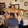 person, cat, indoor, orange_cat, bandana, holding, portrait, clock, dreamcatcher, painting, wall_decor, watch, pajama_pants, home, furniture, relaxed, smile, long_cat, cozy, lights