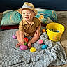 baby, child, hat, straw_hat, smiling, sitting, blanket, easter_eggs, yellow_bucket, colorful, pillow, indoor, happy, toy, floor, cute, playful, young_child, infant, portrait