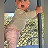baby, child, standing, table, pole, outdoor, leafy_background, curious, surprised_expression, pink_pants, long_sleeve_shirt, barefoot, daylight, shade, portrait, person, young_child, cute, playful, balcony