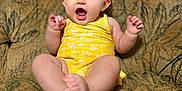 Willow is registered to the contest to win money with this photo: baby, child, clothing, couch, cute, expression, face, feet, hands, happy, indoor, infant, patterned_fabric, person, portrait, sitting, skin, smiling, yellow_dress, young_child