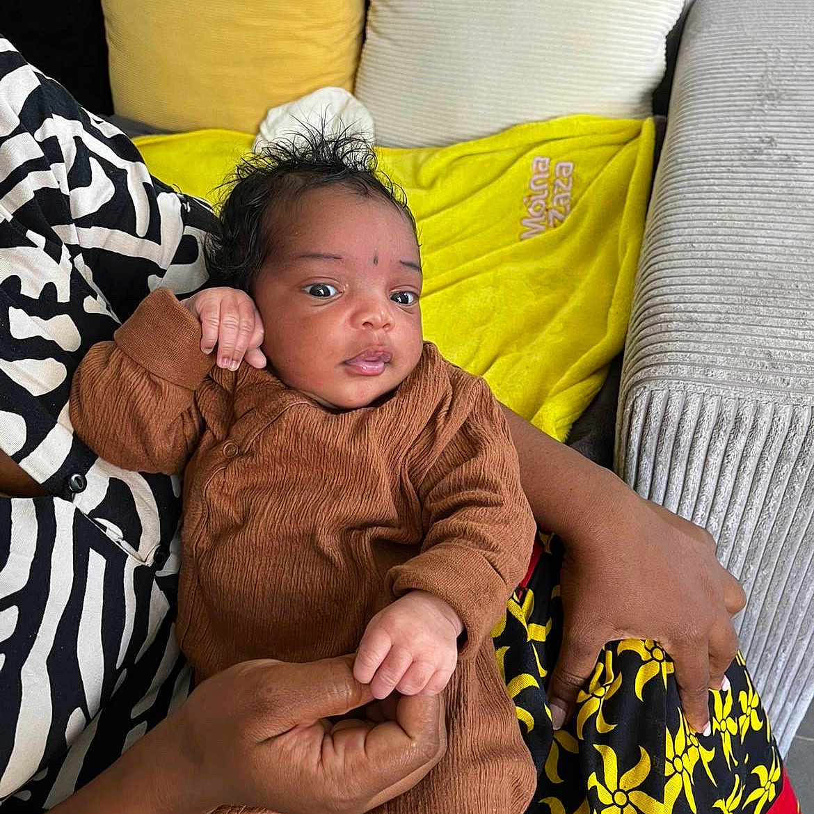 Nayra a rejoint le concours — aidez-le/la à gagner de superbes lots ! baby, blanket, clothing, colorful, comfort, couch, cute, face, hair, hand, holding, indoor, infant, patterned_clothing, person, pillow, relaxation, seated, skin, textile