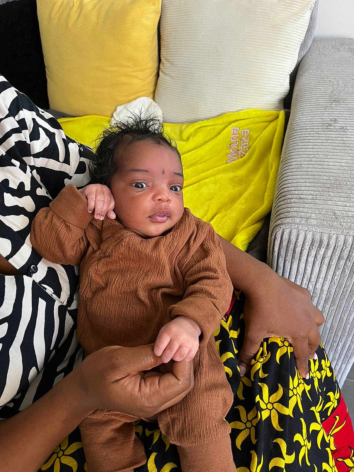 Nayra a rejoint le concours — aidez-le/la à gagner de superbes lots ! baby, infant, person, hand, clothing, couch, pillow, blanket, patterned_clothing, indoor, skin, face, hair, holding, seated, textile, colorful, comfort, relaxation, cute