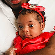 Nayra a rejoint le concours — aidez-le/la à gagner de superbes lots ! baby, infant, red_dress, headband, jewel, adult_hand, white_shirt, closeup, curious_expression, portrait, skin, face, holding, child, person, cute, indoors, newborn, human, love