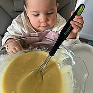 Valentina participe au concours pour gagner de l'argent avec cette photo : child, baby, toddler, highchair, bowl, whisk, batter, cooking, kitchen, utensil, hand, face, expression, apron, bib, table, glass_bowl, food, closeup, parenting