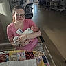 baby, blanket, chair, cradle, glasses, holding, hospital, hospital_room, indoor, infant, medical_equipment, mother, newborn, nursery, patchwork_quilt, person, pink_shirt, smile, visitor_badge, woman