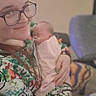 Mazikeen joined the competition — help win amazing prizes! adult, baby, newborn, infant, person, portrait, glasses, smiling, holding, cuddling, indoor, chair, blanket, floral_clothing, patterned_clothing, seated, family, cozy, photograph, soft_focus