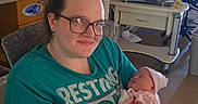 Mazikeen joined the competition — help win amazing prizes! woman, baby, newborn, hospital_room, medical_equipment, glasses, tshirt, chair, crib, mother, infant, holding, seated, bracelet, furniture, indoor, person, portrait, resting, care