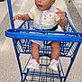 baby, child, shopping_cart, store, floor, clothing, footwear, curious, wide_eyes, jewelry, bracelet, necklace, indoor, retail, aisle, person, cute, pastel_colors, seated, expression