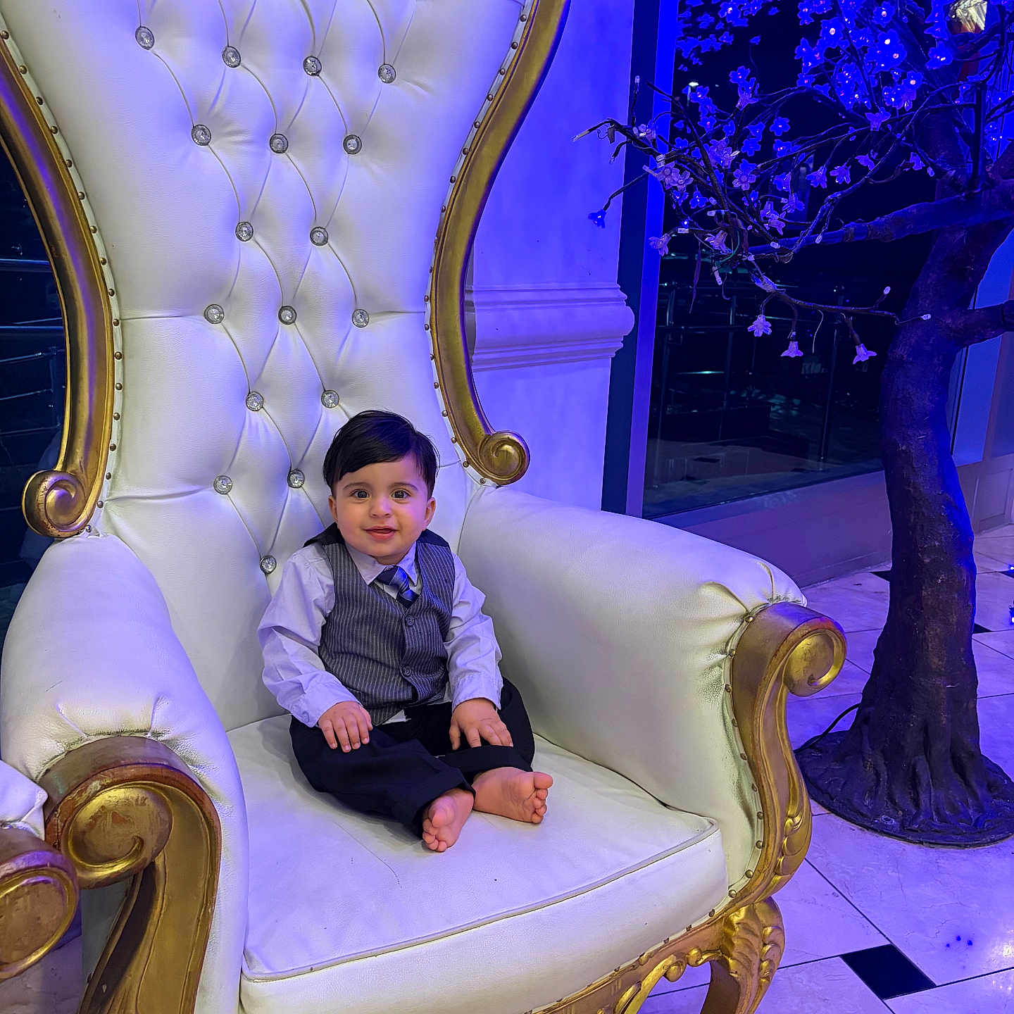 Sayed Emaan is registered to the contest to win money with this photo: barefoot, blue_lighting, chair, child, cute, decorative_tree, formal_clothing, gold, indoor, luxury, marble_floor, ornate, person, portrait, smile, throne, tie, toddler, vest, white