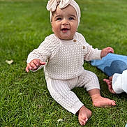 Billie joined the competition — help win amazing prizes! baby, child, grass, outdoor, knitted_clothing, headband, bow, smiling, sitting, person, barefoot, cute, happy, infant, nature, daylight, casual, young_child, greenery, supporting_hand