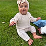 baby, child, grass, outdoor, knitted_clothing, headband, bow, smiling, sitting, person, barefoot, cute, happy, infant, nature, daylight, casual, young_child, greenery, supporting_hand