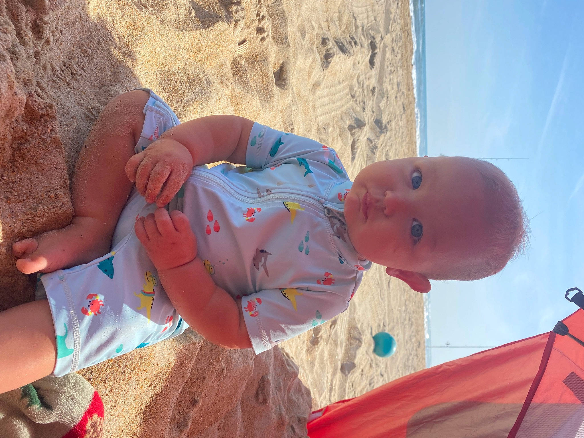 Beckham is registered to the contest to win money with this photo: abdomen, azure, baby, beach, child, elbow, fun, happy, human_leg, landscape, leisure, person, play, recreation, sitting, skin, sky, soil, thigh, toddler