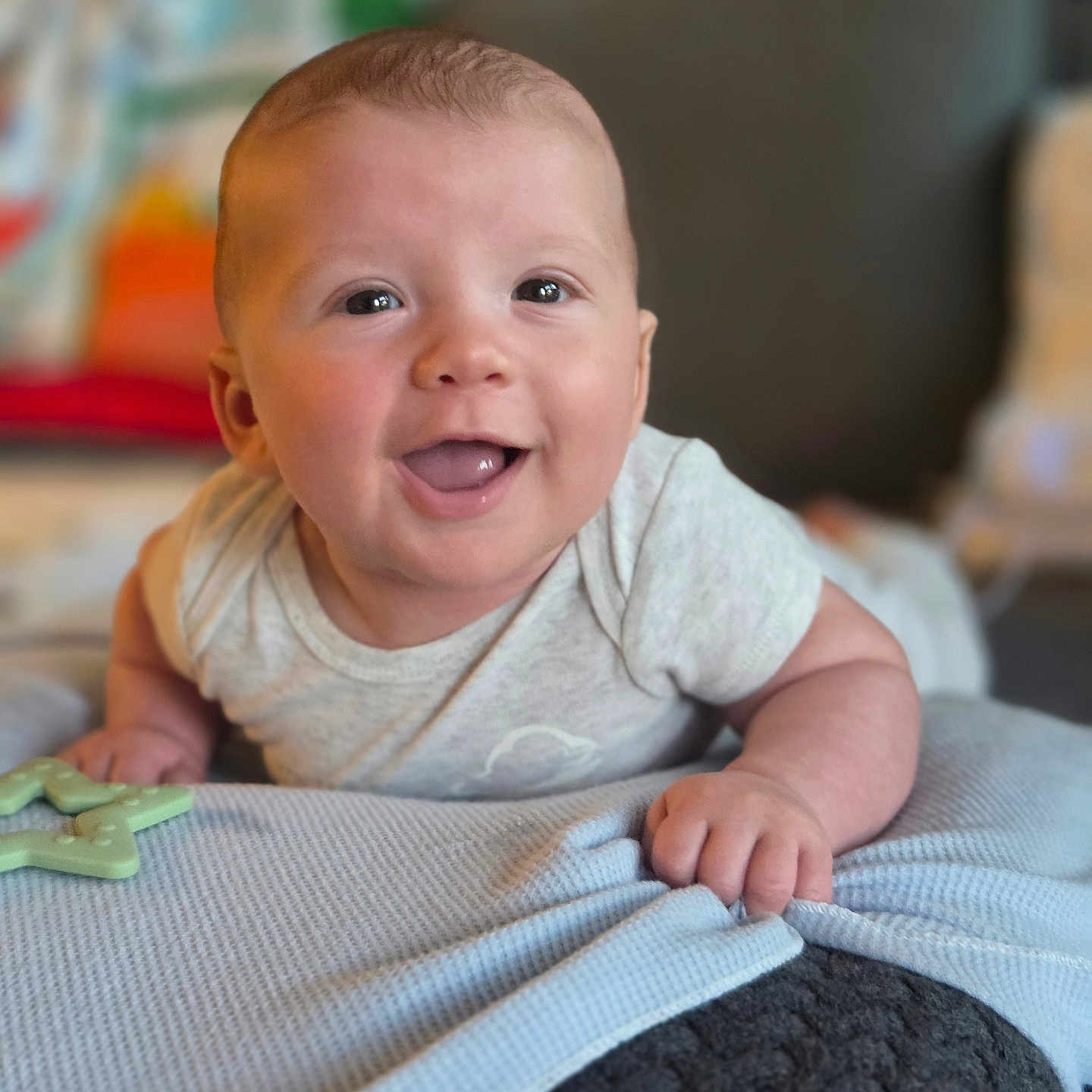 Ozlo joined the competition — help win amazing prizes! baby, infant, smiling, happy, lying_down, blanket, toy, blue, face, cute, child, indoors, person, skin, clothing, hand, head, expression, tummy, background_blur