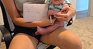 Ozlo joined the competition — help win amazing prizes! baby, woman, indoor, chair, person, smile, holding, paper, pen, carpet, shorts, striped_shirt, skin, face, arm, hand, foot, doorway, light_switch, home
