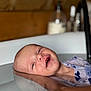 baby, bathtub, water, hand, infant, floating, skin, person, relaxation, bath, wooden_background, blurred_background, smiling, closeup, support, child, indoor, cleanliness, hygiene, soft_lighting