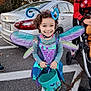 adult, antennae, autumn, butterfly_wings, car, celebration, child, costume, curly_hair, festive, fun, halloween_bucket, happy, holiday, outdoor, parking_lot, person, smiling, stroller, trick_or_treat