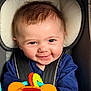 Nick is registered to the contest to win money with this photo: baby, child, car_seat, toy, smile, face, blue_clothing, infant, seatbelt, happy, closeup, indoors, cute, playful, head_support, bright_colors, portrait, young_child, cheerful, baby_toy