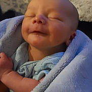 Westyn is registered to the contest to win money with this photo: baby, newborn, infant, sleeping, smiling, blanket, blue_blanket, swaddle, wrapped, face, closed_eyes, arm, hand, soft_texture, couch, sofa, living_room, carpet, portrait, peaceful