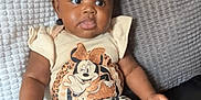 True is registered to the contest to win money with this photo: baby, child, infant, sitting, couch, pillow, headband, clothing, minnie_mouse, patterned_pants, leopard_print, cute, indoor, portrait, young_child, comfortable, expression, black_leather, texture, adorable