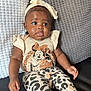 baby, child, infant, sitting, couch, pillow, headband, clothing, minnie_mouse, patterned_pants, leopard_print, cute, indoor, portrait, young_child, comfortable, expression, black_leather, texture, adorable