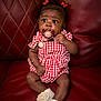 True joined the competition — help win amazing prizes! baby, child, pacifier, red_leather_couch, checkered_outfit, socks, flower_decoration, hair_clips, infant, cute, sitting, indoor, portrait, adorable, young_child, skin, face, expression, clothing, furniture