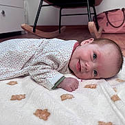 Lya participe au concours pour gagner de l'argent avec cette photo : baby, infant, smiling, blanket, teddy_bear_pattern, floor, wooden_floor, rocking_chair, pink_bag, face, hand, clothing, long_sleeve, indoor, cute, child, portrait, resting, tongue_out, lying_down