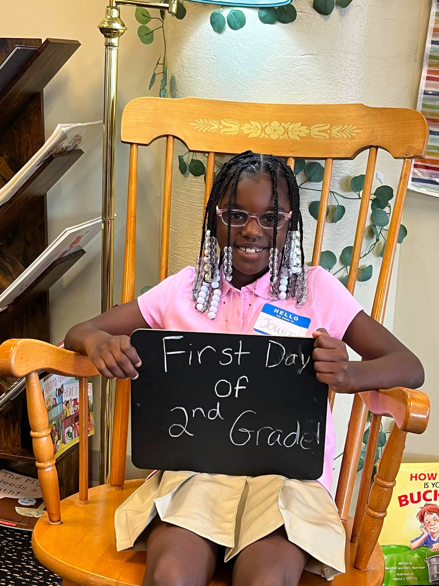 Journee is registered to the contest to win money with this photo: blackboard, bookcase, chair, child, event, eyewear, fashion_accessory, fun, green, handwriting, happy, hat, joy, person, photograph, room, shelf, sitting, smile, snapshot