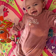 Lucie a rejoint le concours — aidez-le/la à gagner de superbes lots ! baby, infant, smiling, playmat, toy, pacifier, onesie, pink, flower_pattern, butterfly, plush_toy, happy, lying_down, portrait, face, head, cute, nursery, soft_toy, colorful