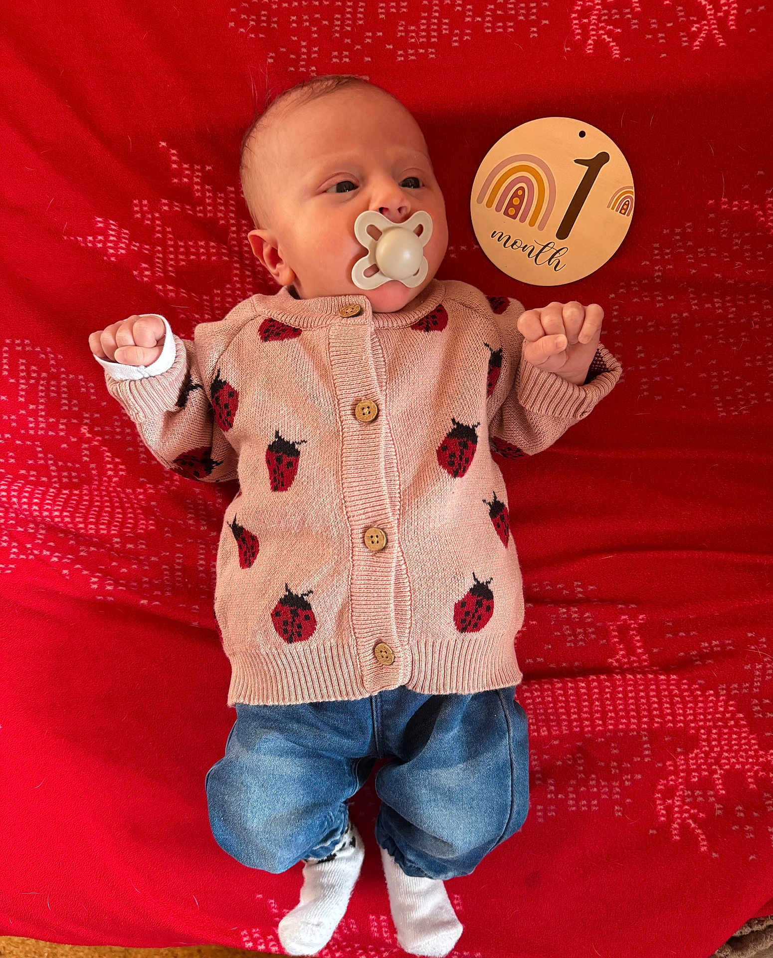 Cassidy participe au concours pour gagner de l'argent avec cette photo : baby, infant, pacifier, sweater, ladybug_pattern, denim_pants, socks, red_blanket, wooden_sign, one_month, cute, newborn, lying_down, portrait, indoors, child, clothing, face, hands, feet