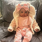 Katelyn joined the competition — help win amazing prizes! baby, infant, pink_clothing, headband, bow, couch, pillow, soft_toys, indoor, smiling, cute, child, portrait, sitting, cozy, warm_clothing, toddler, face, person, home