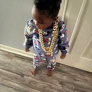 Ezra is registered to the contest to win money with this photo: toddler, child, pajamas, gold_chain, indoor, floor, door, standing, clothing, footwear_barefoot, person, cute, young, home, wood_floor, patterned_clothing, jewelry, smiling, hair, portrait