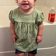 Raelynn is registered to the contest to win money with this photo: toddler, child, smile, green_dress, hair_bows, checkered_shoes, bathroom, bathtub, floor_mat, shorts, standing, happy, indoor, person, cute, small_hands, wall_tiles, skin, socks, eyebrows