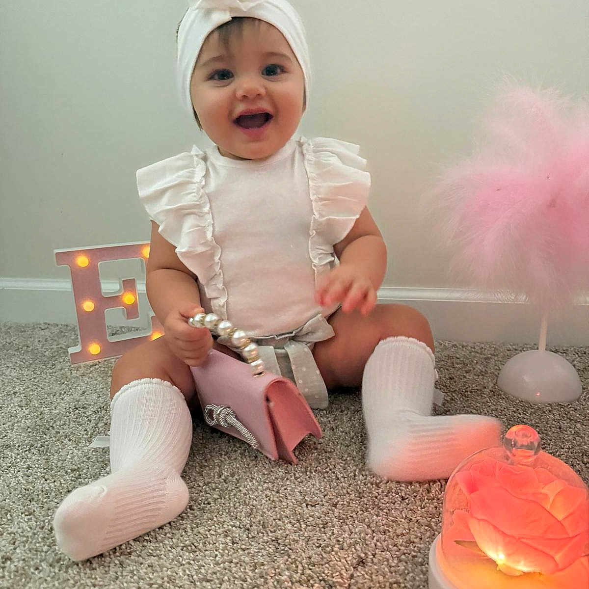 Eilah joined the competition — help win amazing prizes! baby, carpet, child, cute, decor, glass_dome, glowing_flower, happy, headband, indoor, infant, letter_e, portrait, purse, sitting, smiling, sock, soft_lighting, toddler, white_clothing