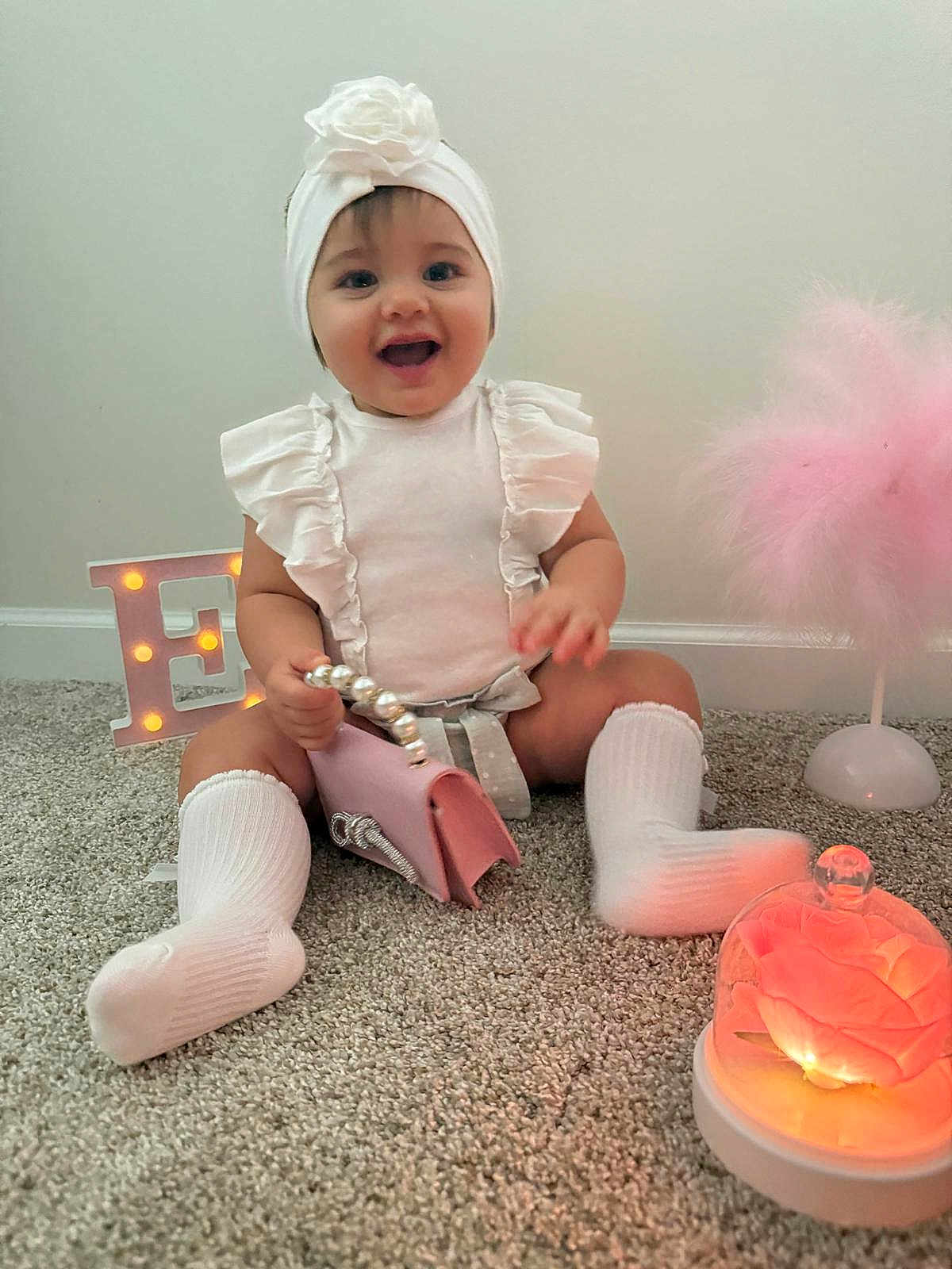 Eilah joined the competition — help win amazing prizes! baby, child, smiling, white_clothing, headband, carpet, purse, decor, glowing_flower, glass_dome, letter_e, indoor, cute, sitting, sock, happy, portrait, infant, toddler, soft_lighting