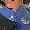 baby, blue_clothing, closeup, comfort, cute, eyes_open, face, family, floral_pattern, head, heart_graphic, indoors, infant, love_text, newborn, person, skin, sleepy, snuggling, tenderness