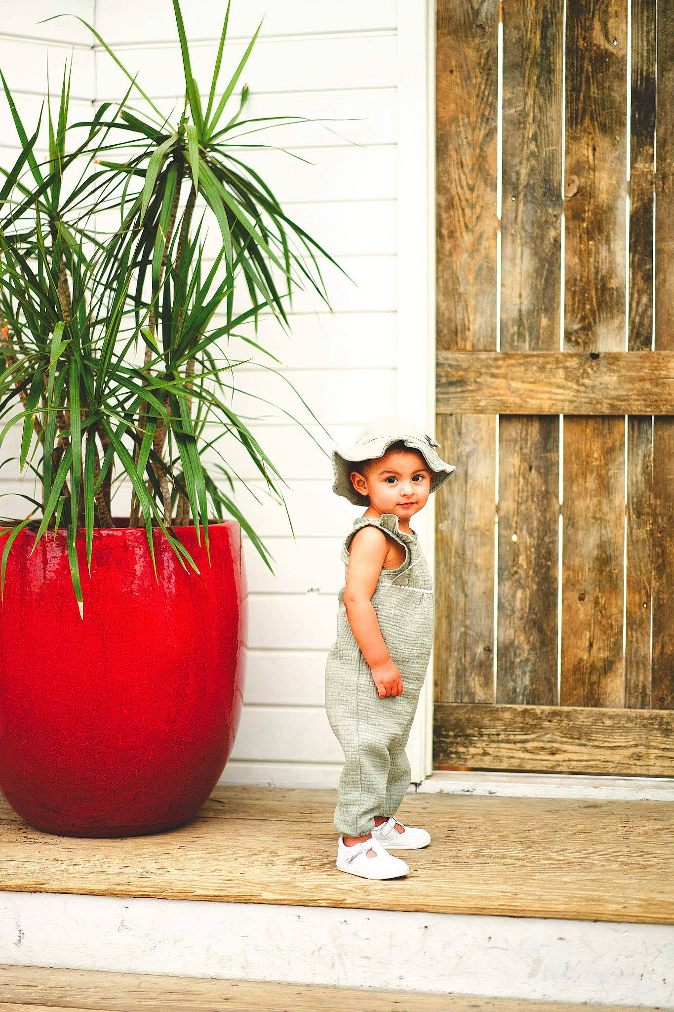 Azaria is registered to the contest to win money with this photo: arecales, child, door, flooring, flowerpot, grass, happy, hat, houseplant, leaf, leisure, person, plant, sandal, sitting, terrestrial_plant, toddler, tree, wall, window