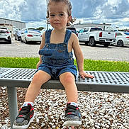 Echeniel is registered to the contest to win money with this photo: toddler, child, bench, denim_overalls, sneakers, nike, curly_hair, outdoor, parking_lot, gravel, grass, cloudy_sky, cars, metal_bench, casual_clothing, person, summer, daylight, portrait, cute