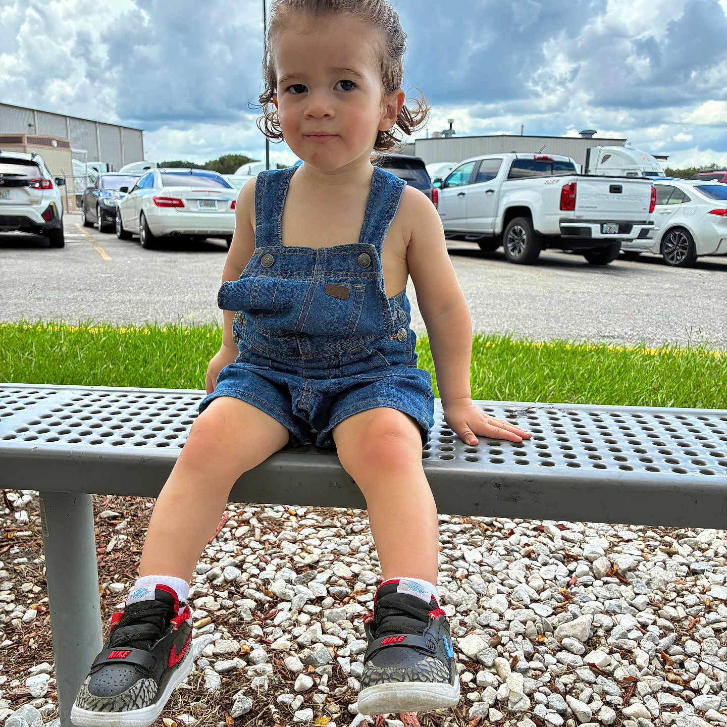 Echeniel is registered to the contest to win money with this photo: bench, cars, casual_clothing, child, cloudy_sky, curly_hair, cute, daylight, denim_overalls, grass, gravel, metal_bench, nike, outdoor, parking_lot, person, portrait, sneakers, summer, toddler