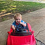 toddler, child, toy_car, red_car, outdoor, sidewalk, grass, building, playful, blonde_hair, concrete, daylight, person, casual_clothing, smiling, fun, summer, nature, cute, small_child