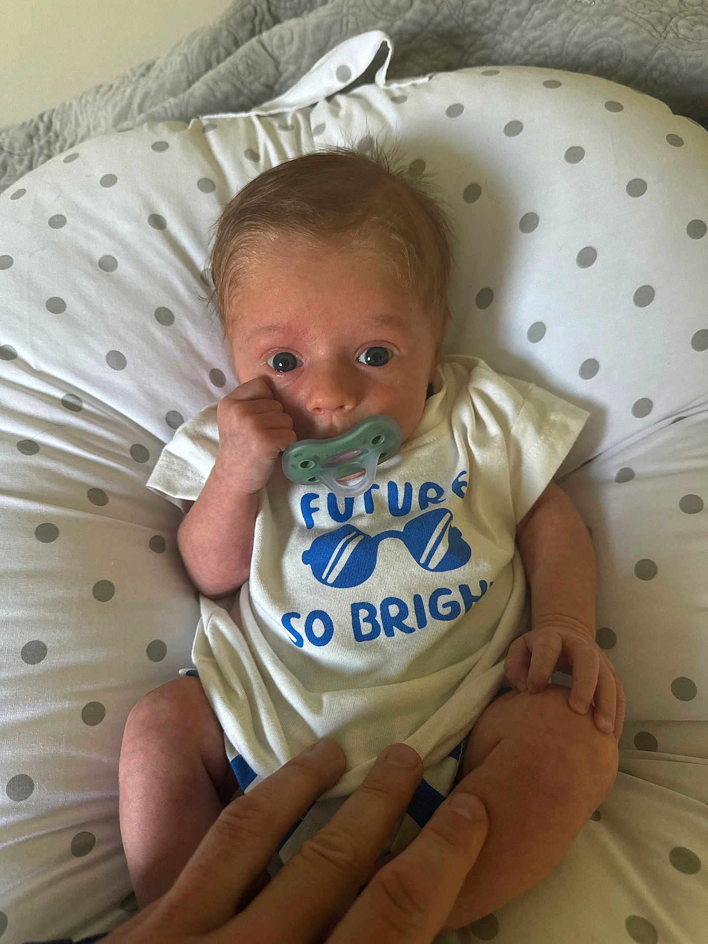 Cullen is registered to the contest to win money with this photo: baby, pacifier, infant, cushion, polka_dot, white_shirt, blue_text, hand, skin, fingers, clothing, cute, child, newborn, lying_down, indoor, human, portrait, small, comfort