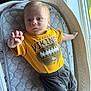 baby, infant, toddler, yellow_shirt, minnesota_vikings, football_graphic, lying_down, baby_lounger, cushion, gray_padded_mat, window_light, curious_expression, hand_reaching, indoor, soft_light, baby_clothes, red_hair, small_feet, cozy, child