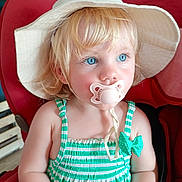 Ella participe au concours pour gagner de l'argent avec cette photo : baby, blonde_hair, blue_eyes, child, close_up, cute, face, green, hat, indoor, pacifier, person, portrait, red_chair, sitting, smiling, striped_dress, toddler, white, young_child