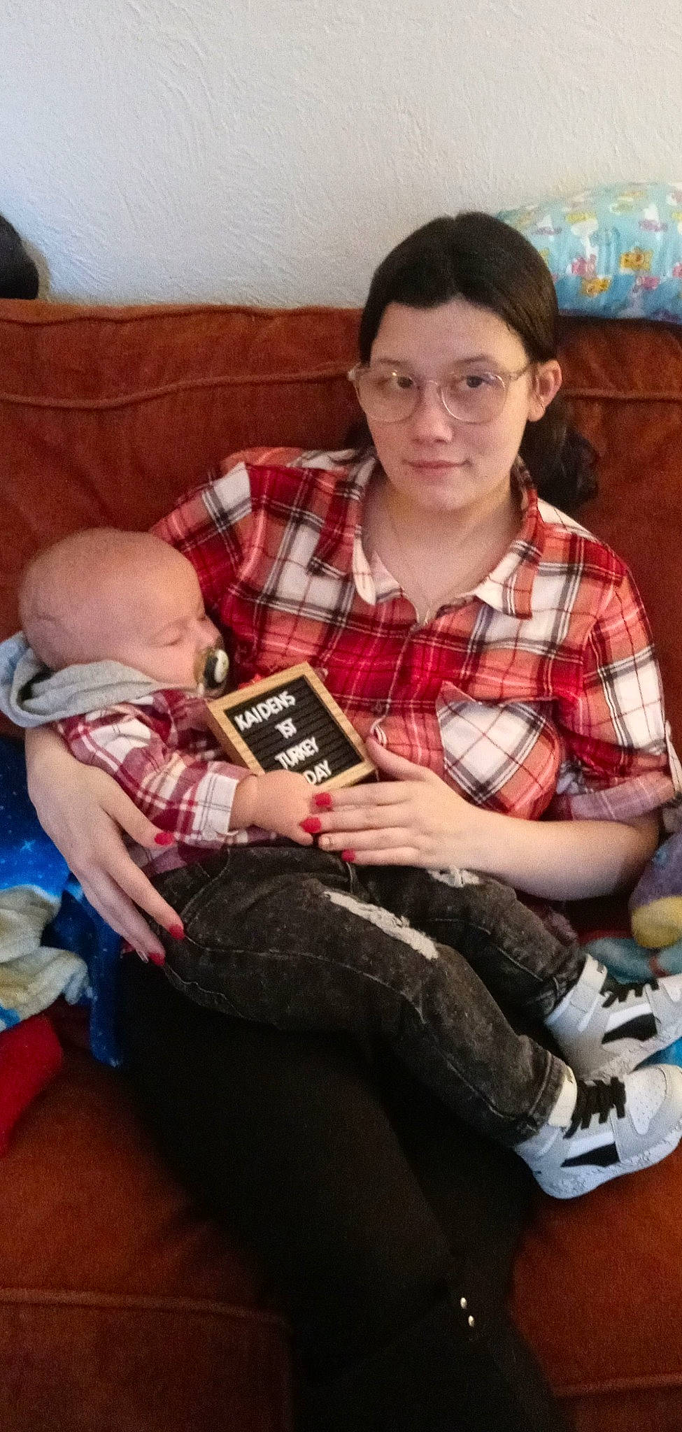 Kaiden is registered to the contest to win money with this photo: baby, book, child, comfort, couch, event, fun, hairstyle, knee, lap, leg, living_room, pattern, person, plaid, room, sitting, sock, tartan, thigh